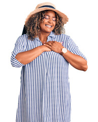 Young african american plus size woman wearing summer hat smiling with hands on chest with closed eyes and grateful gesture on face. health concept.