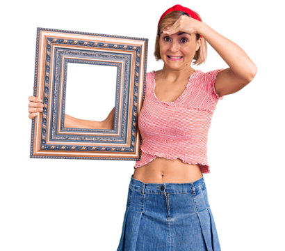 Young blonde woman holding empty frame stressed and frustrated with hand on head, surprised and angry face
