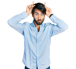 Hispanic man with blue eyes wearing business shirt doing funny gesture with finger over head as bull horns