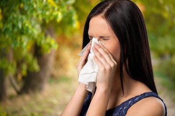 Young pretty woman blowing nose in front of blooming tree. Spring allergy concept. Sick people allergy or virus influenca concept.