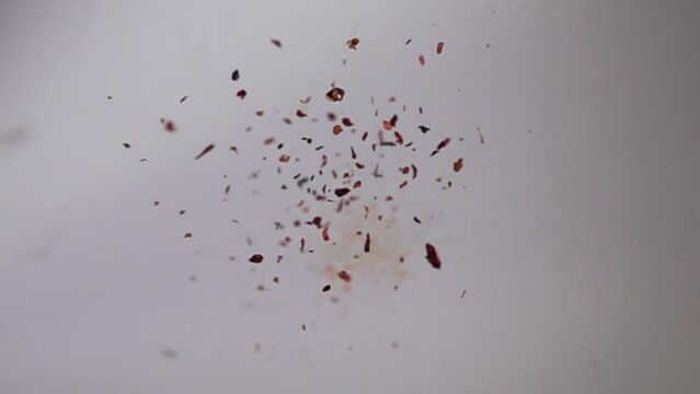 Chili pepper flakes jumping and falling on white surface at super slow motion selective focus shot.