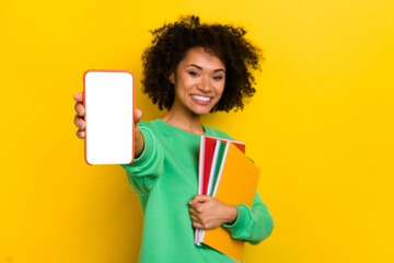 Photo of cheerful charming girl hold show empty space telephone screen isolated on yellow color background