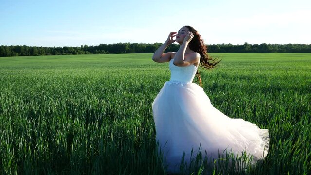 Bride fixes her hair while standing in the middle of wheat field. Wedding dress sways in the wind.