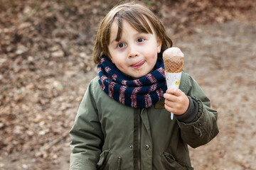 Toddler boy wearing warm jacket and scarf eating chocolate ice cream in waffle  cone with pleasue, ...