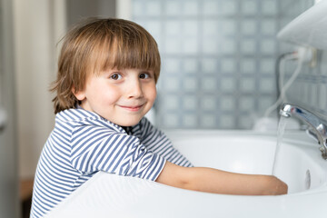 Fototapeta premium Toddler boy wearing striped t-shirt washing his hands in the bathroom. Child hygiene concept.