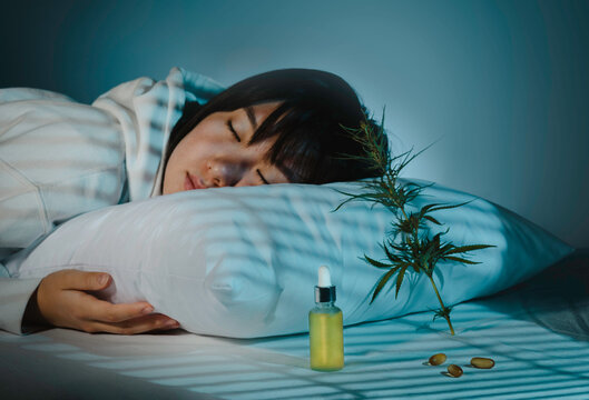 Asian girl sleeping in evening bedroom with cbd oil, capsules and a cannabis branch. Melatonin production, concept of combat sleep disorders