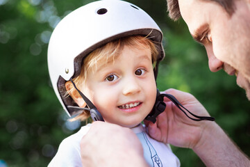 Father putting on his toddler son protective helmet, family activities outdoor. Child safety.