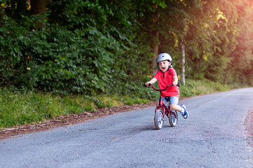 Toddler boy riding down on a balance bike in the park in summer.  Sport activity for little children.