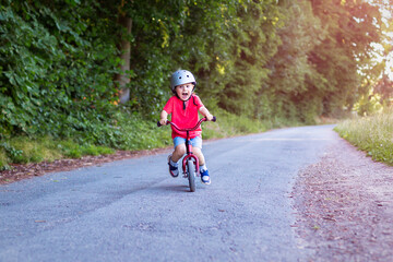 Toddler boy riding down on a balance bike in the park in summer.  Sport activity for little children.