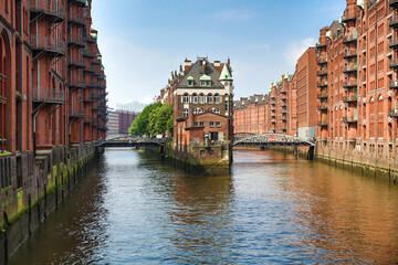 Foto von Hamburg Altstadt. Rote alte Reihenhäuser, verbunden durch Brücken. Sie liegen auf ruhigem Wasser, Kanäle. Darüber der klare wolkenlose Himmel. Bäume hinter den Häusern. Europäische Stadt.