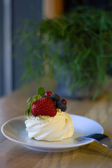 A delicate Pavlova topped with fresh berries sits on a plate, ready to be enjoyed in a casual yet elegant setting