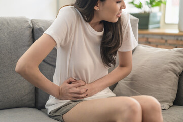 Fototapeta na wymiar Healthcare medical or daily life concept : Close up stomach of young lady have a stomachache or menstruation pain sitting on a sofa.