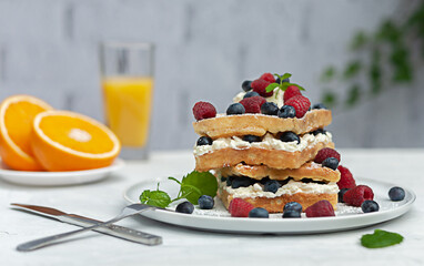 Fresh Viennese or Belgian waffles on a plate with fresh raspberries and blueberries and whipped cream.