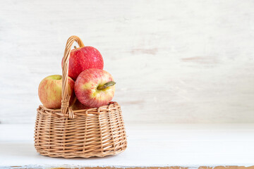 Decorative basket with fresh apples for Christianity Savoir of the Apple Feast Day on white wooden background with copy space.