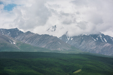 Dramatic aerial view to large snow mountain range under rainy cloudy sky. Dark atmospheric alpine scenery with high snowy mountain peak in low clouds. Gloomy landscape with mountain top in overcast.