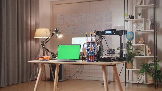 A Laptop With Mock-Up Green Screen Is Next To A Cyborg Hand And 3D Printing On The Table At Home
