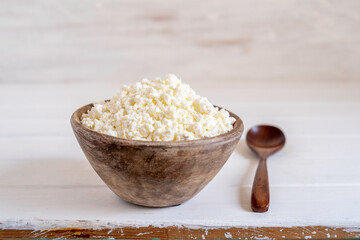 Cottage cheese in wooden bowl over white background. 