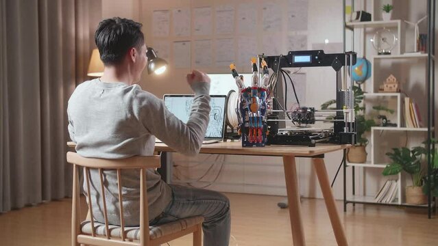 Back View Of A Male With 3D Printing Celebrating Succeed Designing A Cyborg Hand On A Laptop At Home
