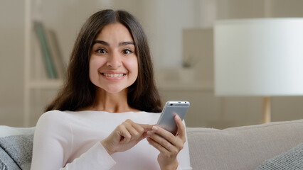 Amazed pretty arab woman girl scrolling pictures likes selfie photos on phone using mobile options...
