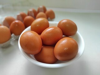 Brown chicken eggs in plastic container and white bowl on white background.