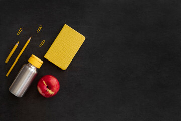 Flatlay, free space, save space. Yellow office supplies, a bottle and a red apple on a black background.