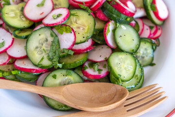 Cucumber Radish Salad on ceramic plate with wooden cutlery. Summer food.