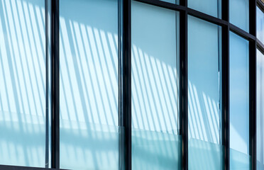 Sunlight and shadow on surface of curve glass building wall with white sunshade inside the office room