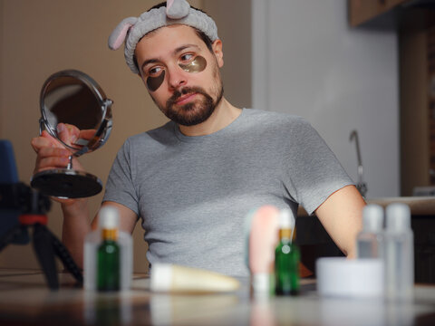 Patches for eyes. Young man in kitchen with headband on his head and mirror apply use under eye anti-wrinkle patches, men do morning facial procedures with hydrogel beauty product, skincare.