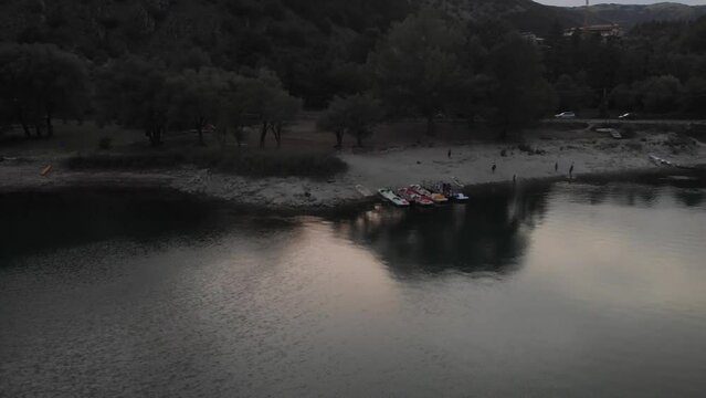 lateral aerial shot of the coast of Lake Scanno with pedal boats moored on the shore at sunset