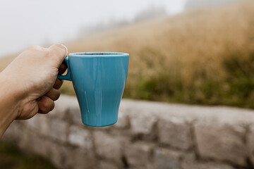 Turquoise mug with coffee on the background of a mountain meadow