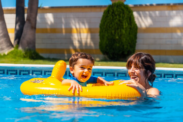 Smiling mother playing with her son with a yellow float in the pool