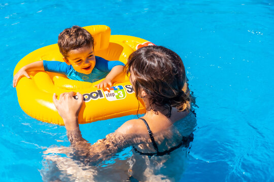 Mother having fun playing with her son with a yellow float in the pool