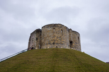 Fototapeta na wymiar View of Clifford's Tower in York, UK with green grass hill and cloudy sky background. No people.
