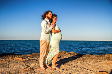 Fototapeta na wymiar A pregnant couple on a beach during sunset