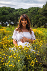 Fototapeta premium A young pregnant woman in a field touching her pregnancy belly