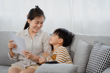 Asian boy, And his mother is working on a laptop computer, The little boy put the tablet in his hand and turned to his busy mother intently, wanting his mother to pay attention to him.