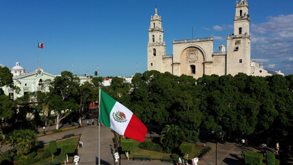 Aerial view in front of Mexican flag waving in front of the cathedral San Ildefonso in Merida, Yucatan, Mexico.