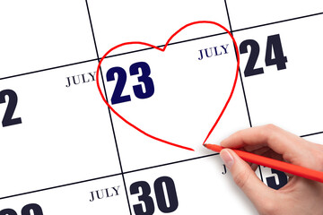 A woman's hand drawing a red heart shape on the calendar date of 23 July. Heart as a symbol of love.