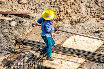A construction worker carries deformed bars for foundation steel work on a very hot day. 