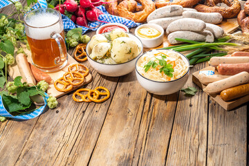 Oktoberfest holiday greeting card, menu, invitation background, Traditional Oktoberfest festival food, bavarian sausages, pretzels, potato, sauerkraut, beer mug on wooden background, copy space above