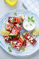 Blue and white plate with grilled watermelon batons, goat cheese and yogurt, middle close-up, vertical shot, high angle view