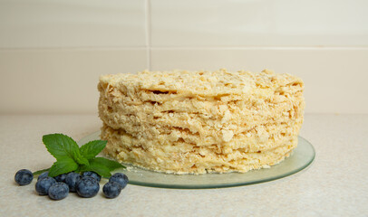 Homemade Napoleon cake is on the table. It is decorated with mint leaves and blueberries
