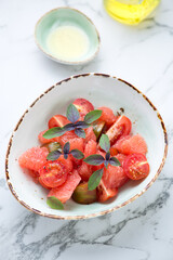 Salad with grapefruit, tomatoes and basil leaves served in a green bowl, vertical shot on a light-grey marble background