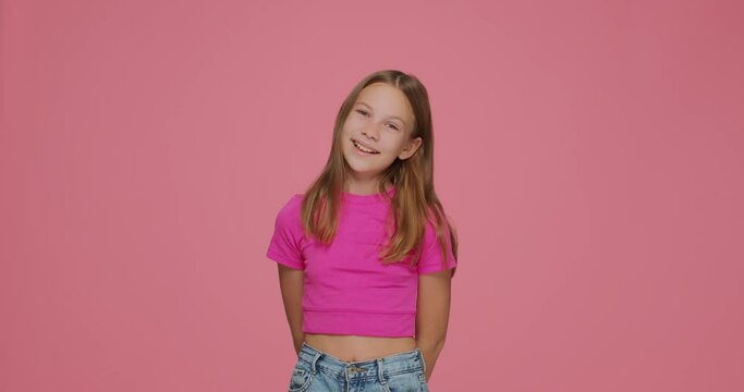 Cute elementary child girl posing, smiling on pink studio background. Childhood, children's online store advertising