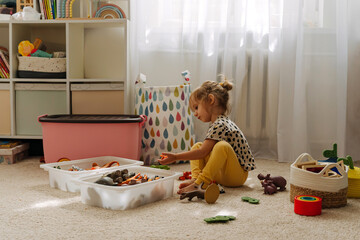 A little girl playing with toy animals and wooden blocks in nursery. Kid and toys with storage...
