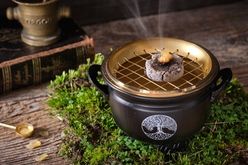 Aromatic frankincense resins on glowing charcoal in a witch cauldron with symbol 
