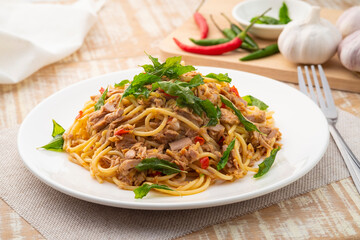 Stir fried Spaghetti with Canned tuna fish and crispy basil leaves in white plate,Spicy pasta Pad Kra Pao.Thai fusion food