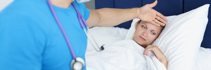 Fototapeta na wymiar Doctor keeps hand on forehead of sick woman on bed