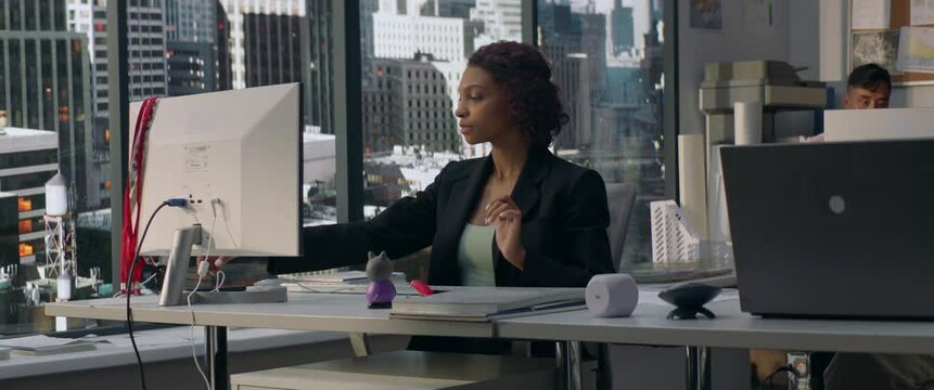 African American female employee working at her desk in the office located in a skyscraper. Modern friendly working environment