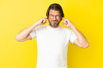 Fototapeta na wymiar Senior dutch man isolated on yellow background frustrated and covering ears